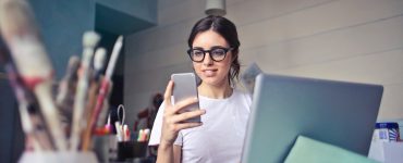 woman in white t shirt holding smartphone in front of laptop 914931